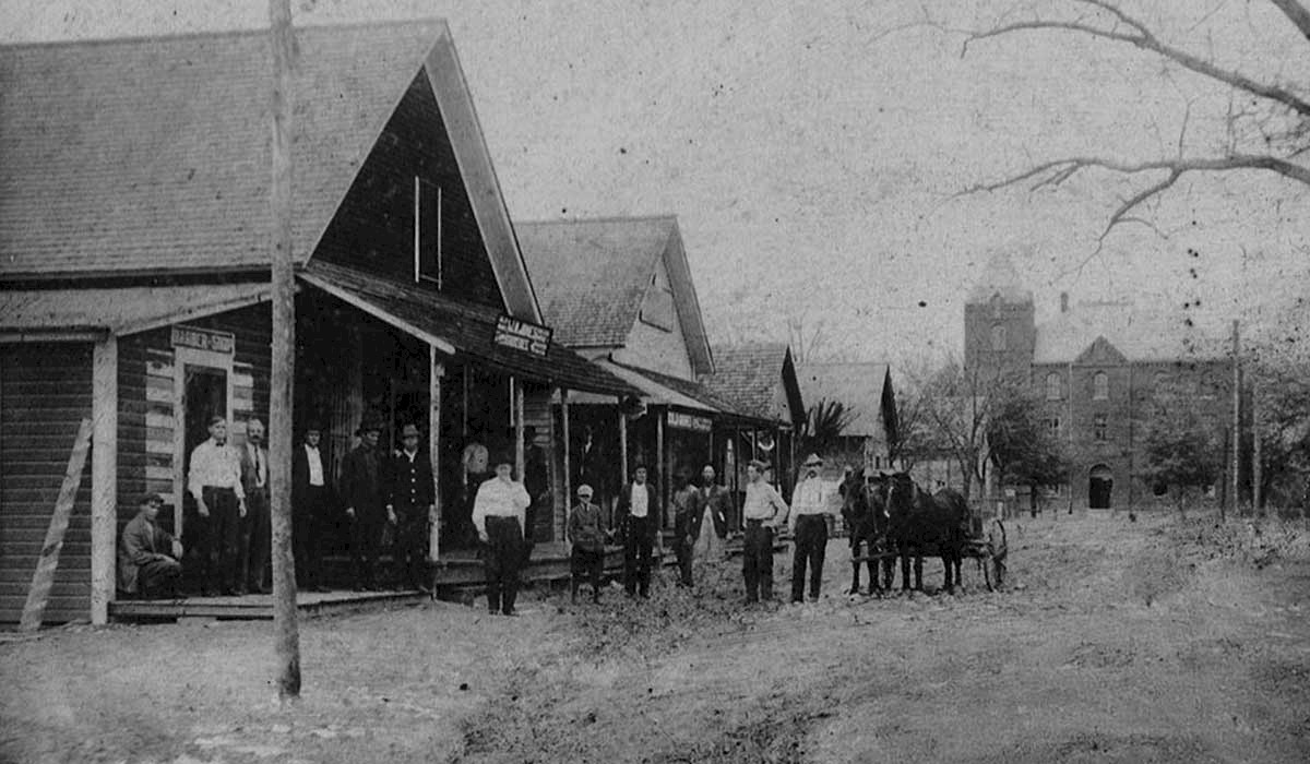 1800s photo of downtown vernon, Florida. Photo shows several men gathered around one of many wooden buildings for that era.